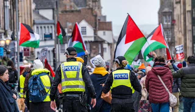 Police officers walk behind protesters carrying Palestinian flags on Edinburgh's Royal mile