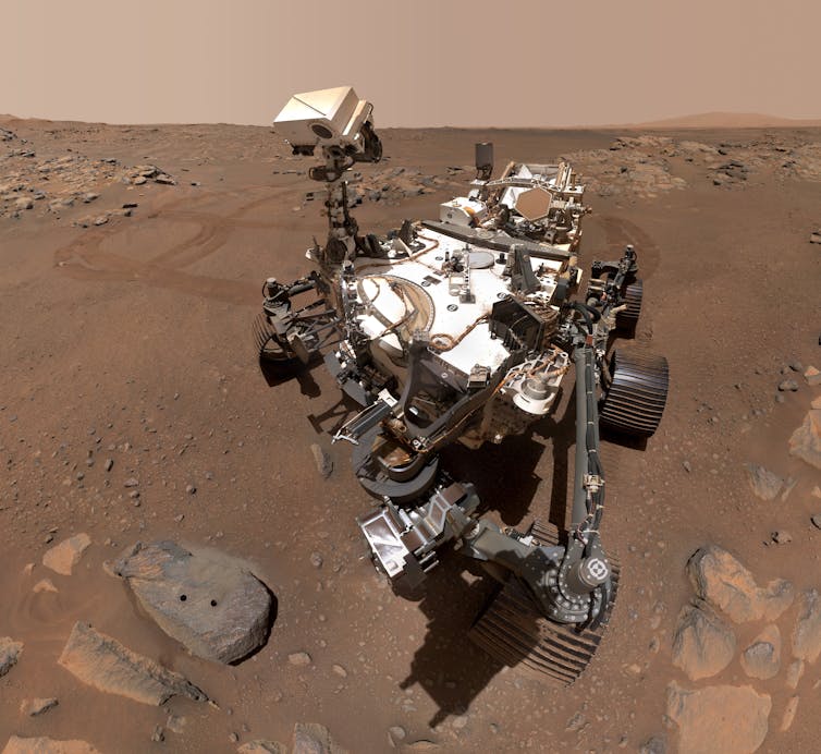 The Perseverance rover, dusty and dirty, parked in a patch of Martian soil.