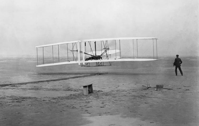 A black and white historical photograph of the first flight of the Wright brothers.
