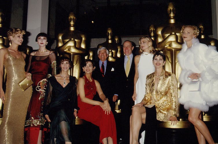 Elegantly dressed women and men pose in front of tall, golden statues.