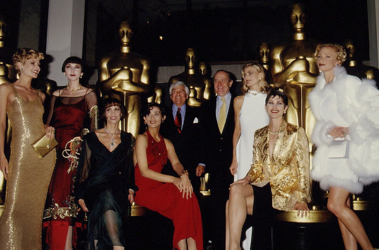 Elegantly dressed women and men pose in front of tall, gold statues.