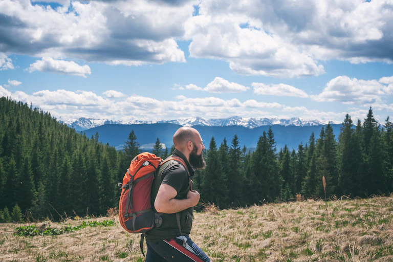 A fit man who is balding is hiking in the wilderness.