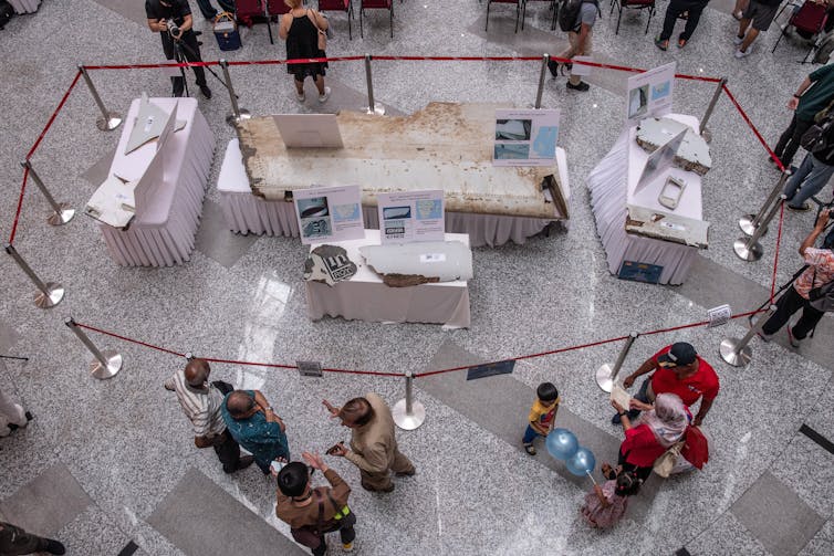 Overhead view of tables with several broken pieces of an aircraft with detailed plaques.