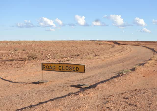 A road curving through the Australian outback with a road closed sign placed across it.