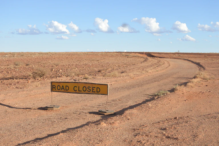 A road curving through the Australian outback with a road closed sign placed across it.