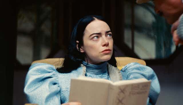 woman with dark hair looks up confused from book (film still)