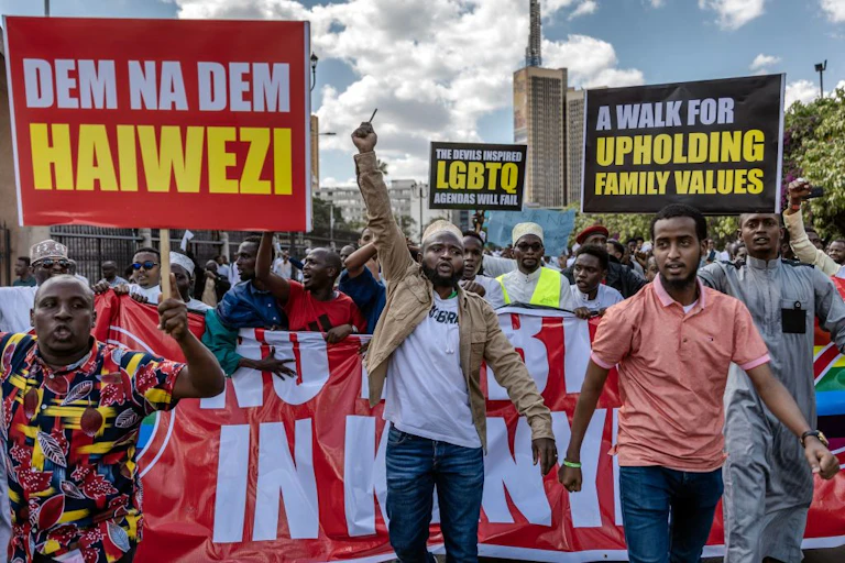 A crowd of protesters marching down a city street with banners that read "A walk for upholding family values", "The devil inspired LGBTQ agenda will fall" and the like.