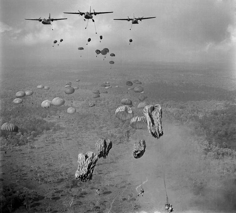 A black and white image of paratroopers jumping out of a plane.