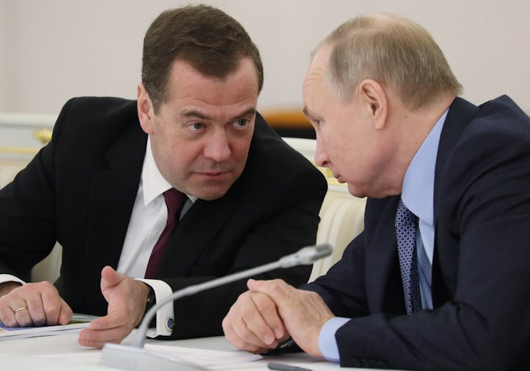 Vladimir Putin and Dmitry Medvedev put their heads together while talking.