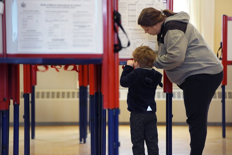 An adult stands with a child at a voting booth.