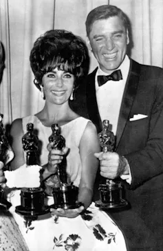 People with Oscar trophies, one in a dress and one in a tuxedo.