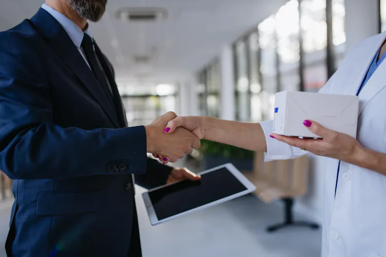A person in a business suit shaking hands with someone in a white coat who is holding a box