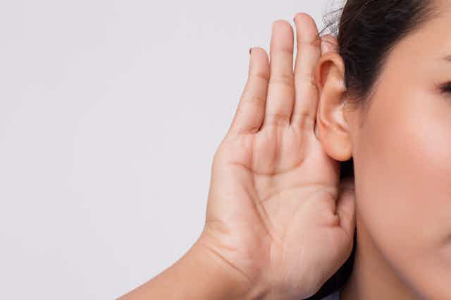 mulher coloca as mãos no ouvido em gesto para tentar escutar melhor