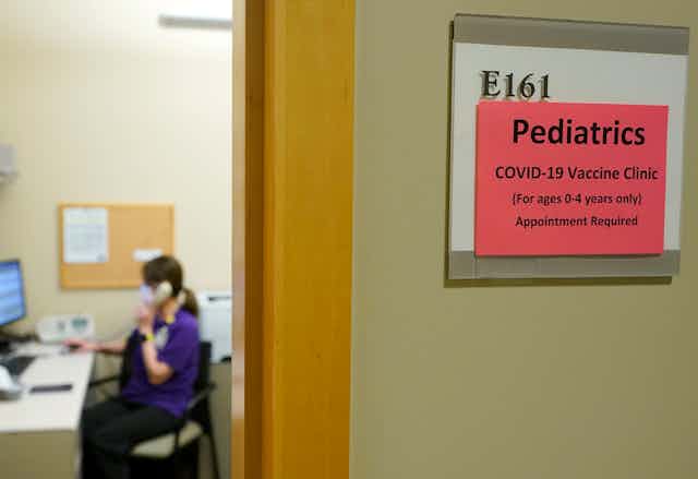 sign for pediatric vaccine clinic outside room with woman in scrubs on phone
