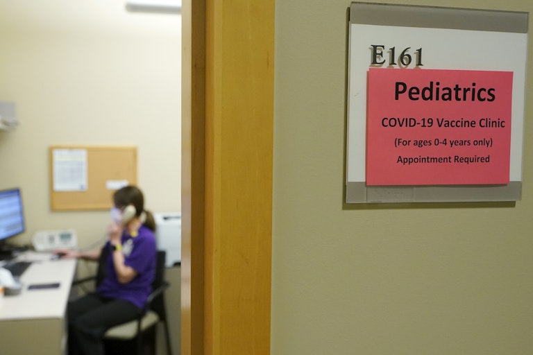 sign for pediatric vaccine clinic outside room with woman in scrubs on phone