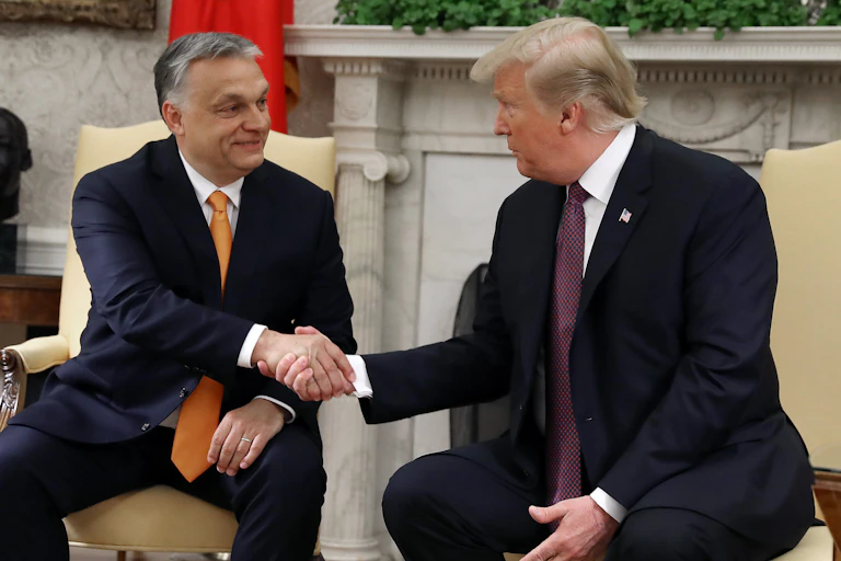 Two men in suits and ties, sitting down and shaking hands.