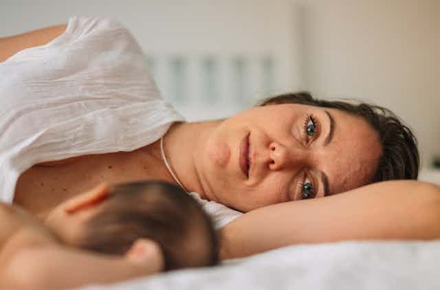 New mum lying on bed, staring into distance, with newborn baby