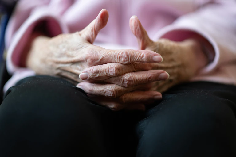 An elderly person's hands are folded in the person's lap.