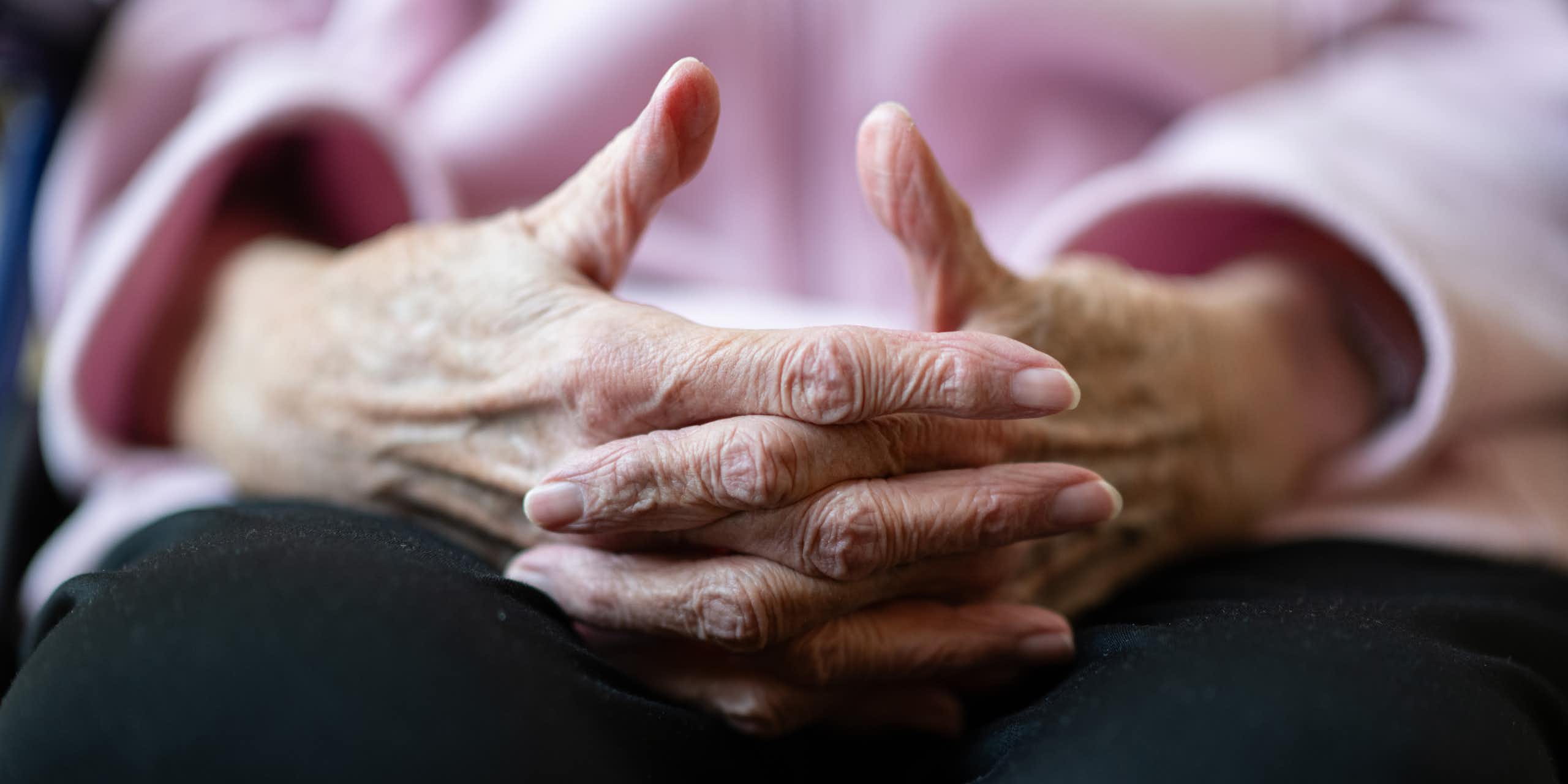 An elderly person's hands are folded in the person's lap.