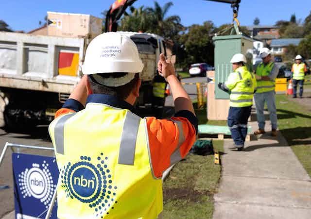 A photo of worked in NBN-labelled hi-vis gear carrying out some kind of works.