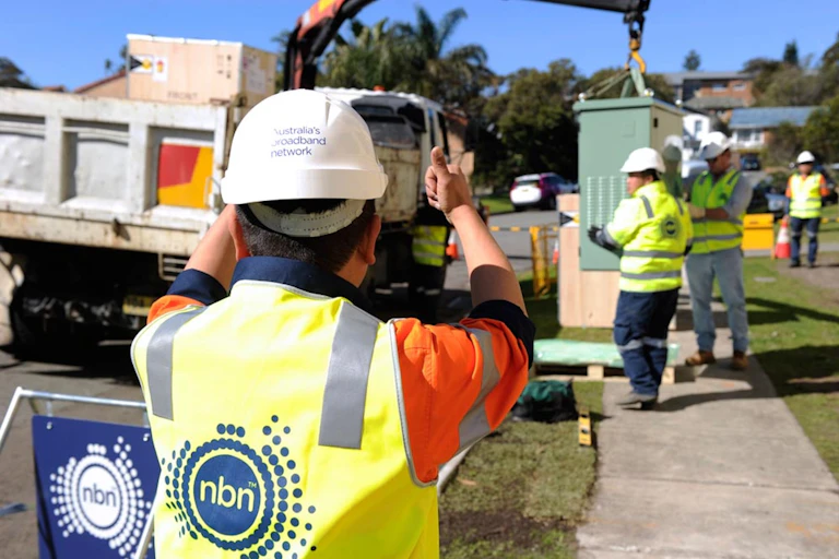 A photo of worked in NBN-labelled hi-vis gear carrying out some kind of works.
