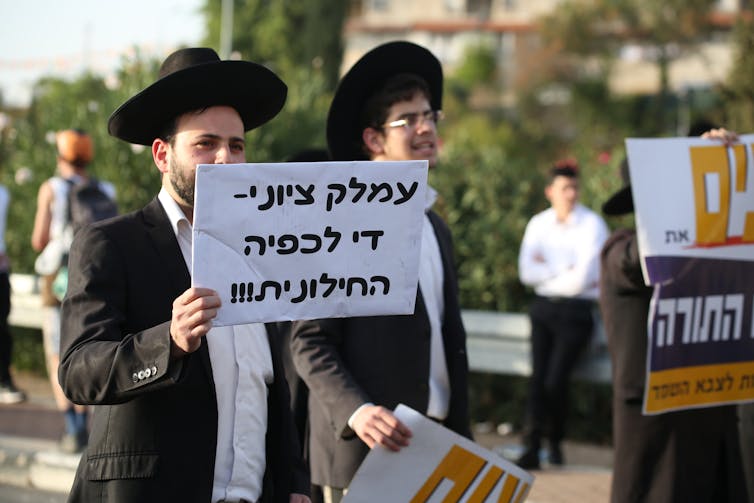 Two ultra-Orthodox men holding signs written in hebrew.