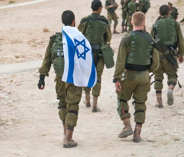 Several Israeli soldiers walking with an Israel flag.