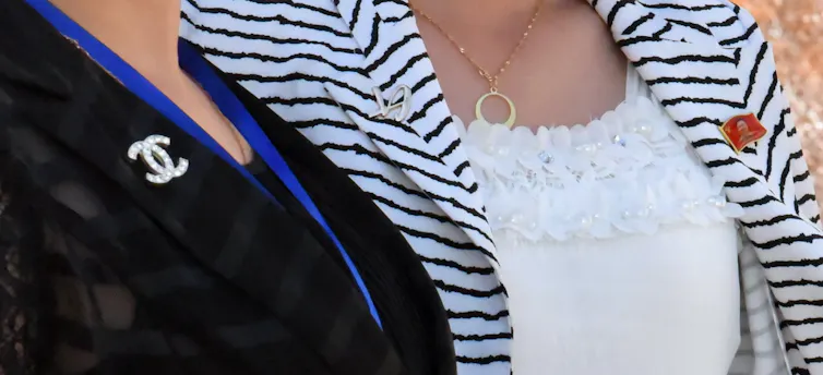 Two women one with a Chanel-style brooch and another with a North Korean label pin.