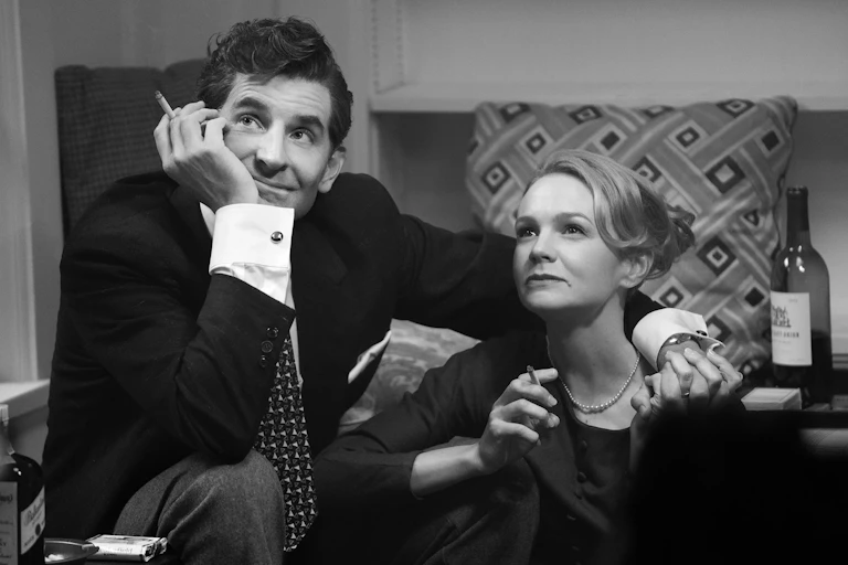 Man holding cigarette rests head on palm while his arm is around a young woman who's cradling a cigarette in her fingers.