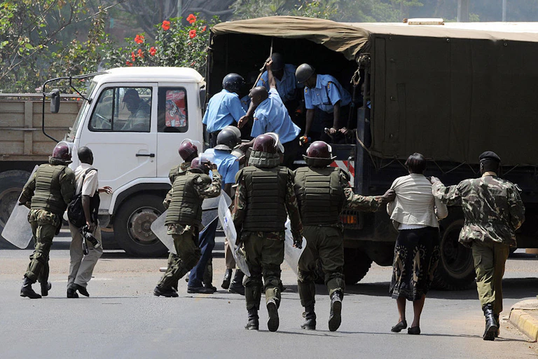 Police in riot gear escort a trio under arrest to a waiting lorry