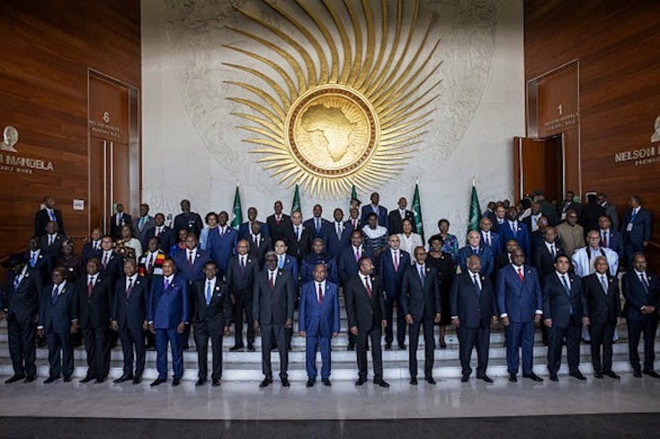 Un groupe d'hommes et quelques femmes posent pour une photo devant le logo de l'Union africaine.