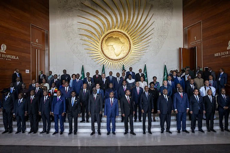 Un groupe d'hommes et quelques femmes posent pour une photo devant le logo de l'Union africaine.