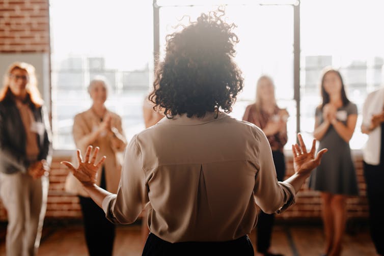 View from behind of a young, black woman speaking to female colleagues in an office