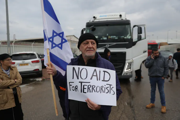 A man stands in front of an aid truck destined for Gaza carrying an Israeli flag and a sign reading: 'No aid for terrorists'.