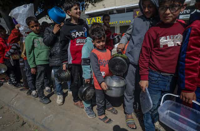 Children carry pots and pans as they queue for aid in trhe Gaza Strip, February 2024.
