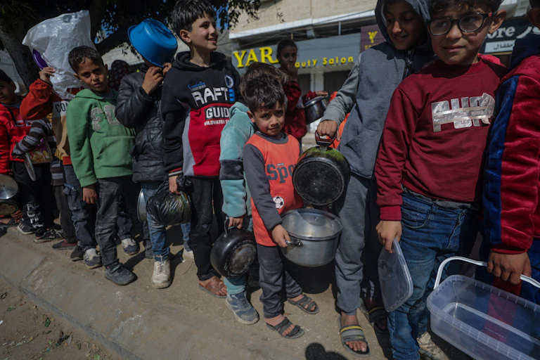Children carry pots and pans as they queue for aid in trhe Gaza Strip, February 2024.