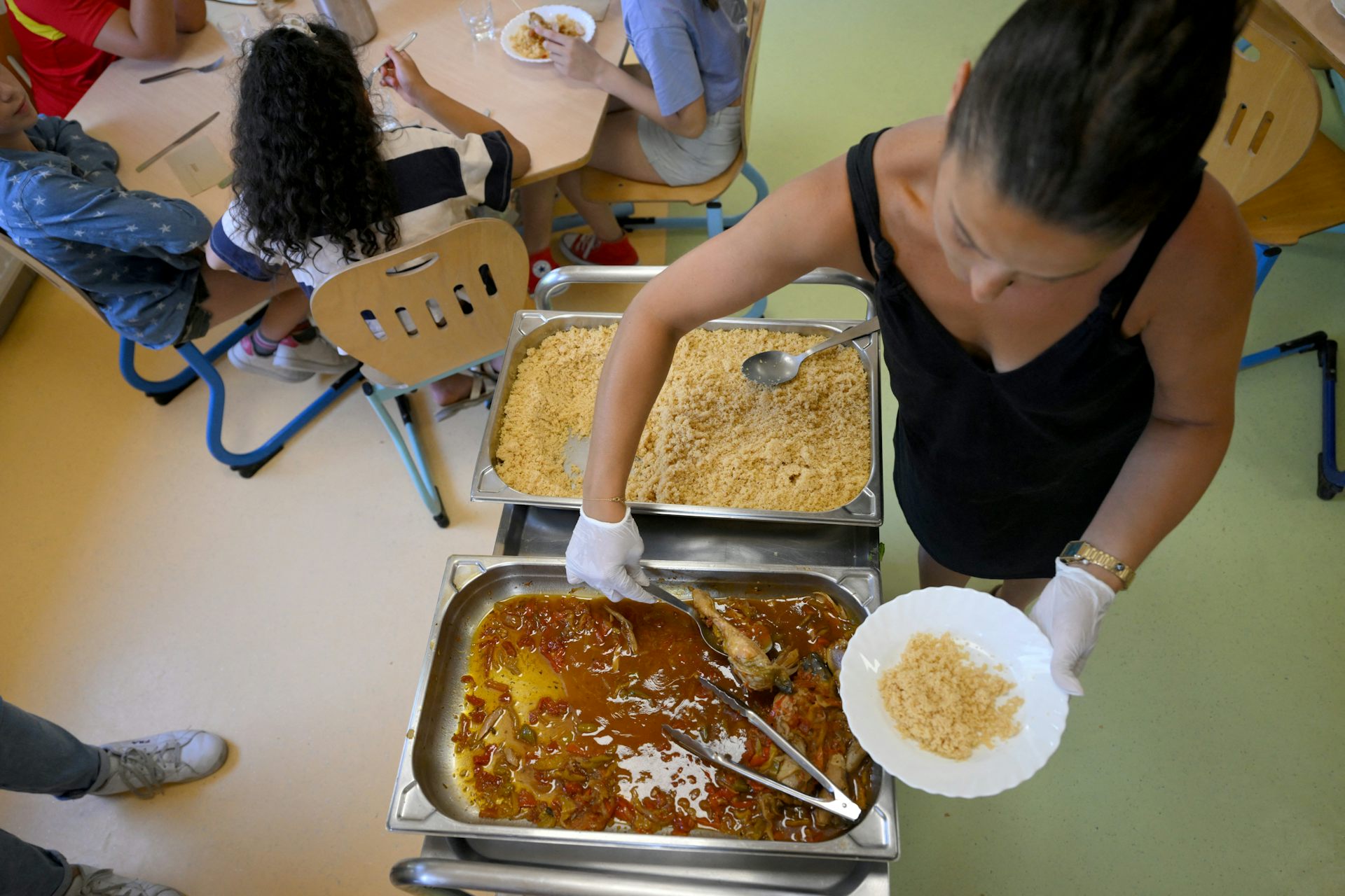 Un employé sert des repas pendant que des enfants déjeunent à la cantine d’une école primaire à Saint-Remy-de-Provence, dans le sud de la France, le 23 juin 2022