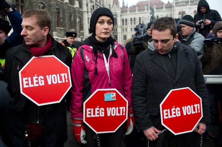 Three people standing before a crowd holding stop signs.