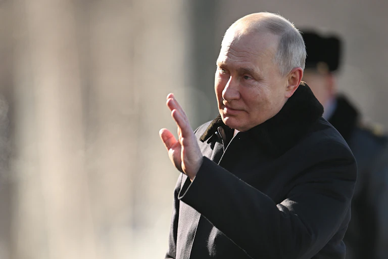 A balding man in a heavy overcoat waves.