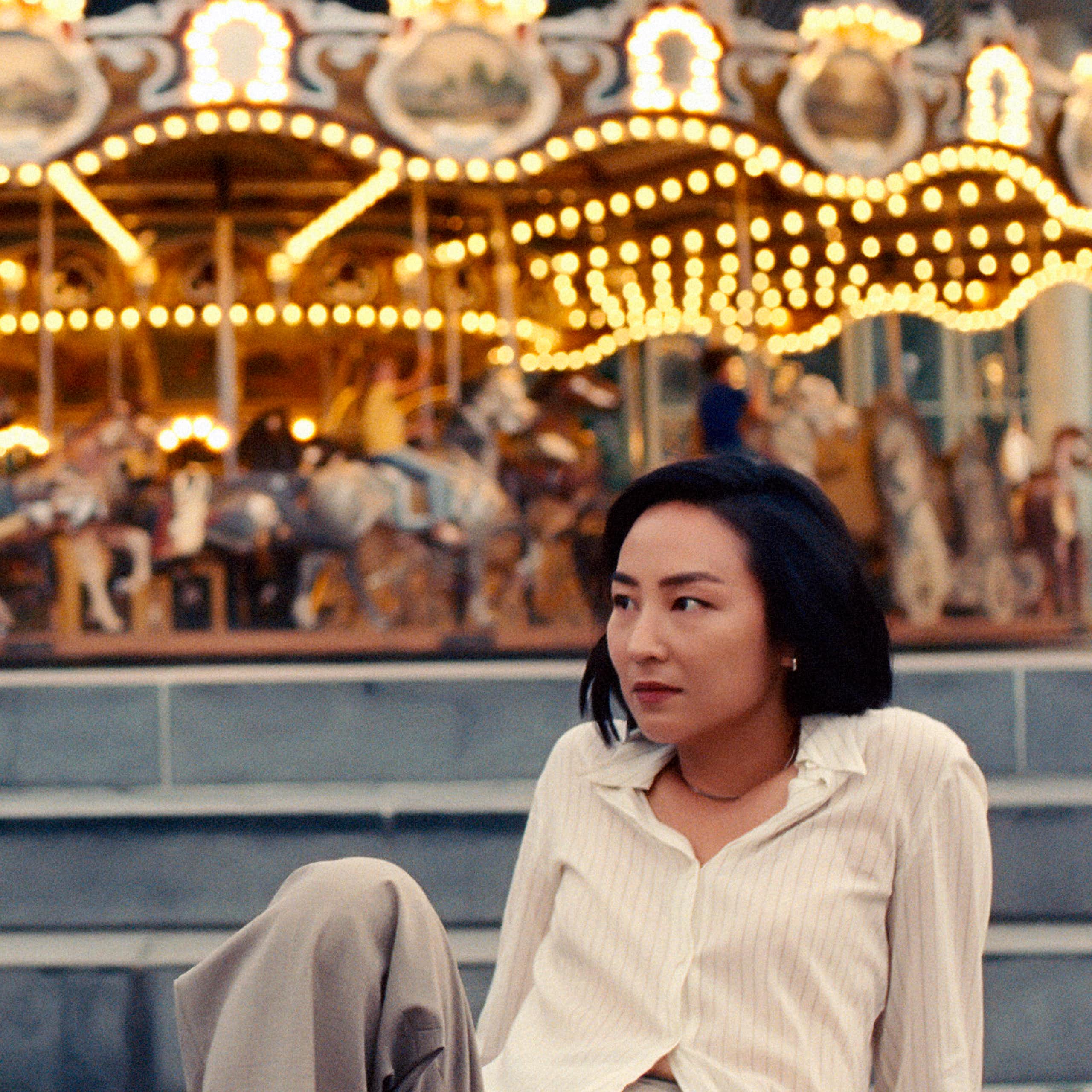 An Asian man and woman sit in front of a merry-go-round