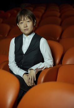 An Asian woman poses for a photo sitting in an orange theatre chair
