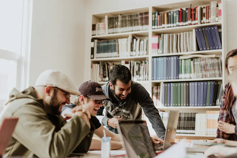 Workers look at a laptop, laughing