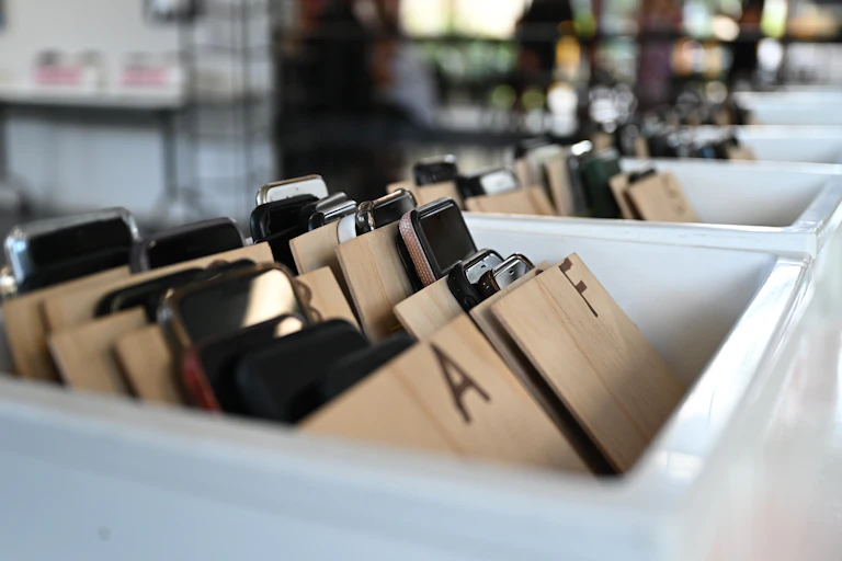 Mobile phones in plastic containers, organised under the alphabet (as part of a school phone ban).