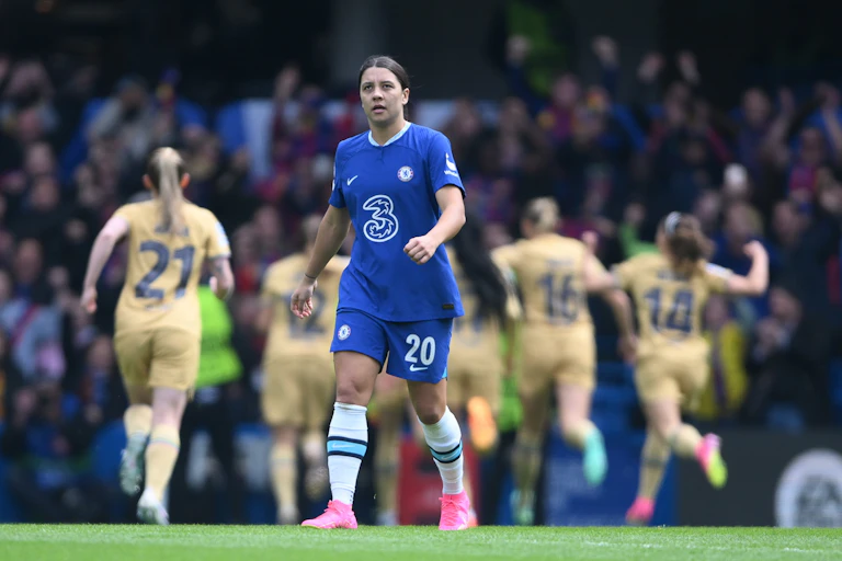 Female footballer in blue kit walks on pitch