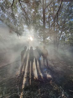 A group of people standing in the bush during a controlled burn, with the sun in the background peeking through the smoke