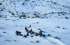 Fotograma de _La sociedad de la nieve_ en el que se ve el avión rodeado de supervivientes en medio de los Andes.