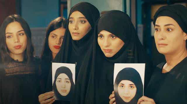 Five women in black attire hold up the photos of two women.