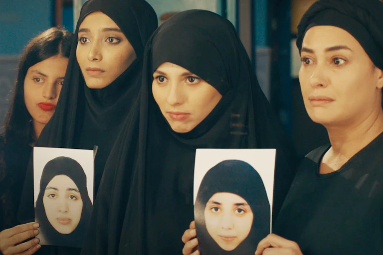 Five women in black attire hold up the photos of two women.