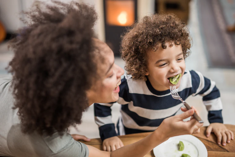 woman holding fork with kiwi in child's mouth