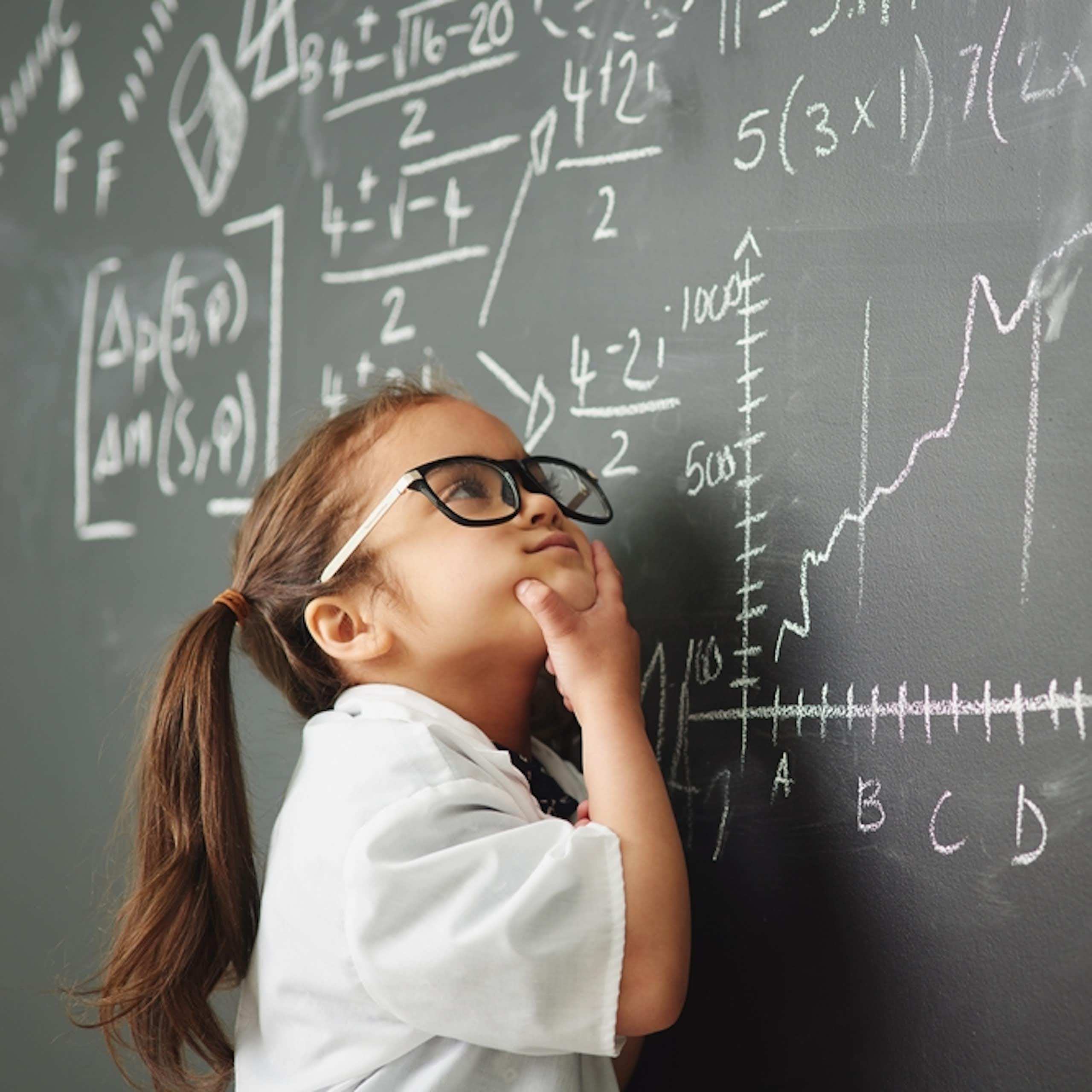 Petite fille avec des lunettes en train de résoudre des équations très compliquées sur un tableau noir dans une classe